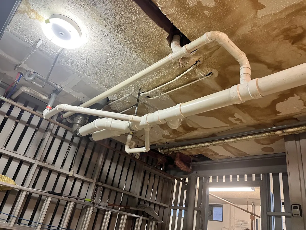 New PVC drain lines run along a basement ceiling