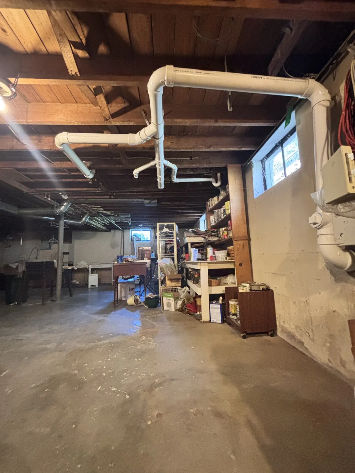New white PVC drain lines along the joists of a basement ceiling