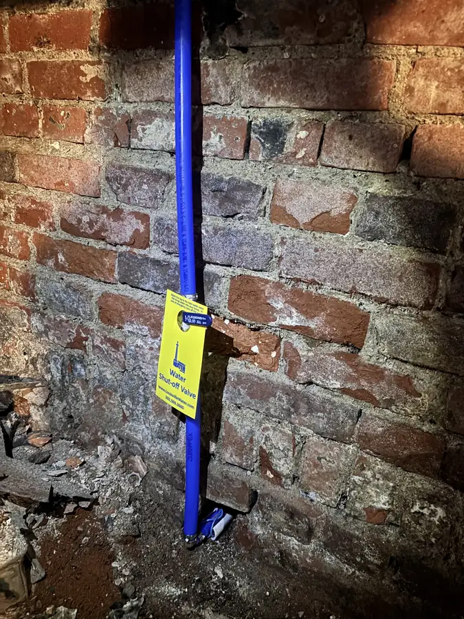 New blue water line at a brick foundation wall with a yellow Louisville Water shut-off valve tag